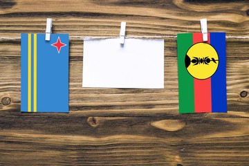 Hanging flags of Aruba and New Caledonia attached to rope with clothes pins with copy space on...
