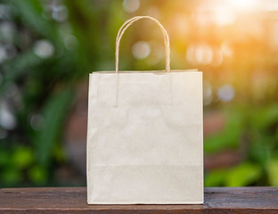 Brown recyclable paper shopping bag Placed on a wooden table, the backdroup is a green tree. For the background image used to campaign, do not use plastic bags.