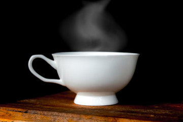 Hot coffee cup on old wooden table in dark background.