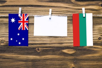 Hanging flags of Australia and Bulgaria attached to rope with clothes pins with copy space on white note paper on wooden background.Diplomatic relations between countries.