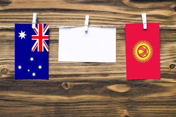 Hanging flags of Australia and Kyrgyzstan attached to rope with clothes pins with copy space on white note paper on wooden background.Diplomatic relations between countries.