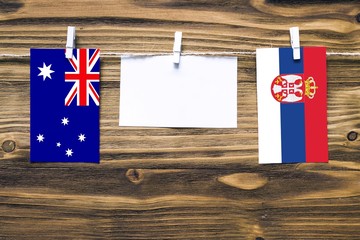 Hanging flags of Australia and Serbia attached to rope with clothes pins with copy space on white note paper on wooden background.Diplomatic relations between countries.