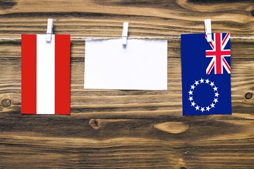 Hanging flags of Austria and Cook Islands attached to rope with clothes pins with copy space on white note paper on wooden background.Diplomatic relations between countries.