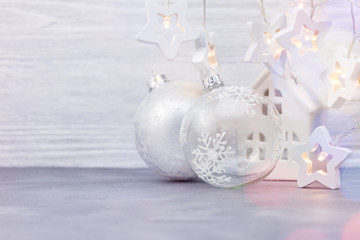 glass christmas tree balls, decorative star garland lights and small house toy on white wooden background