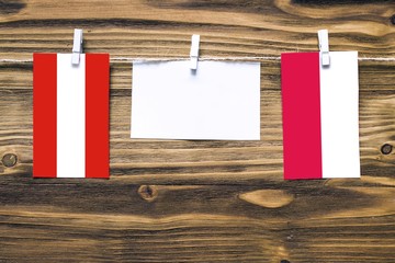 Hanging flags of Austria and Poland attached to rope with clothes pins with copy space on white note paper on wooden background.Diplomatic relations between countries.