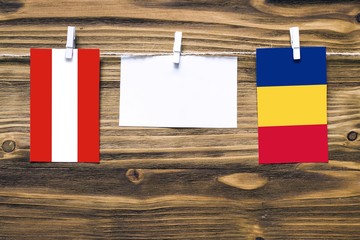 Hanging flags of Austria and Romania attached to rope with clothes pins with copy space on white note paper on wooden background.Diplomatic relations between countries.