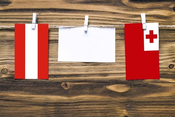 Hanging flags of Austria and Tonga attached to rope with clothes pins with copy space on white note paper on wooden background.Diplomatic relations between countries.