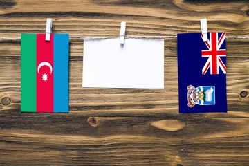 Hanging flags of Azerbaijan and Falkland Islands attached to rope with clothes pins with copy space on white note paper on wooden background.Diplomatic relations between countries.