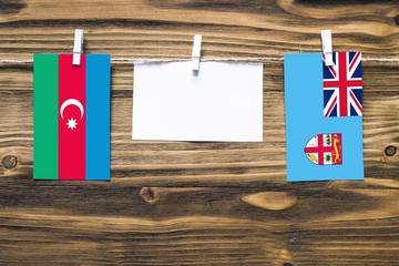 Hanging flags of Azerbaijan and Fiji attached to rope with clothes pins with copy space on white note paper on wooden background.Diplomatic relations between countries.