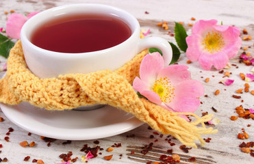 Cup of tea with wild rose flower on old board