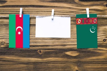 Hanging flags of Azerbaijan and Turkmenistan attached to rope with clothes pins with copy space on white note paper on wooden background.Diplomatic relations between countries.