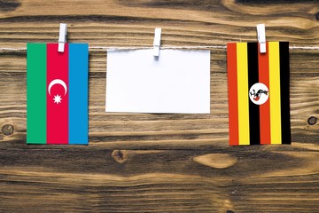 Hanging flags of Azerbaijan and Uganda attached to rope with clothes pins with copy space on white note paper on wooden background.Diplomatic relations between countries.