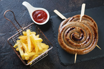 Roasted rolled sausages on skewers with french fries and ketchup, elevated view over dark brown...