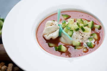 Closeup of cold tomato gazpacho with burrata cheese and cucumber slices, selective focus