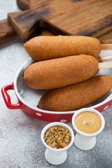 Corn dogs with mustard, vertical shot on a beige stone surface, closeup, selective focus