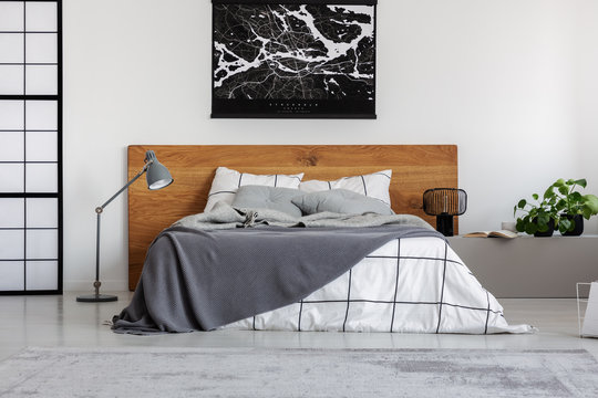 Black map on white wall above wooden headboard in simple bedroom interior