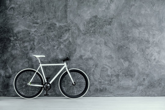 White and black bike on empty grey concrete wall, real photo with copy space