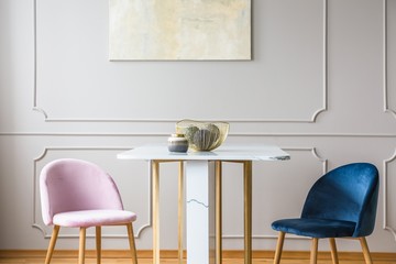 Velvet pastel pink and petrol blue chairs at small dining table in bright living room