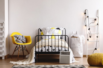 Copy space on empty white wall in classy scandinavian kid's bedroom with single metal bed, yellow chair and paper bag with pillows