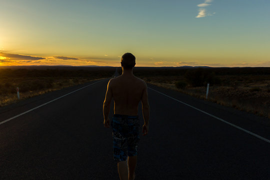 young caucasian man walking on a straight road through the nullarbor dessert of Australia at sunset, South Australia, Australia