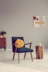 Yellow knot pillow on trendy vintage armchair in empty room
