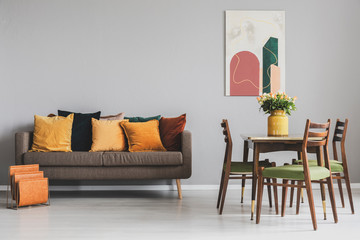 Living and dining room interior with brown sofa and wooden table with vintage chairs