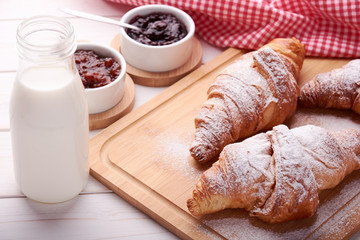 Still life with sugared croissant, porcelain bowls with fruit jam and glass of milk on white wooden table top