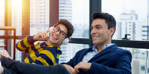 Two New Generation young businessmen who are colleagues work together are chatting in a comfortable atmosphere with a smile in the morning at the modern office surrounded by glass of window.