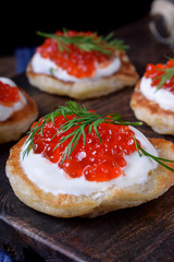 Pancakes with red caviar and cream cheese topped with dill on the wooden board
