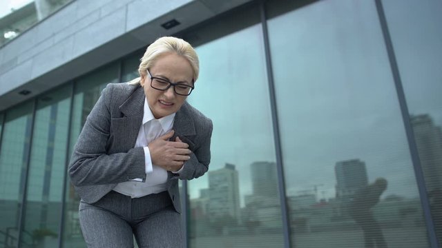 Woman in business suit throwing briefcase feeling strong pain in heart, dystonia