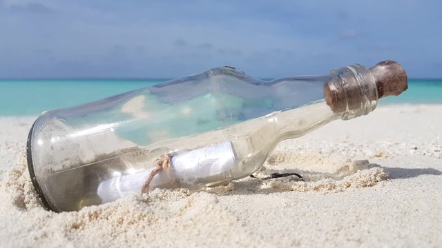 A surprising letter in a bottle came along unexpectedly in the white sand beside the cool green sea in the Philippines - steady shot