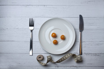 cape gooseberry on the white plate with knife and fork and tape-measure on wooden background flat lay