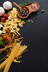 Flat lay Ingredients for cooking Italian pasta on black stone slate - fettuccine, spaghetti, tomatoes, basil, oil and garlic. Italian food. Top view with space for text.