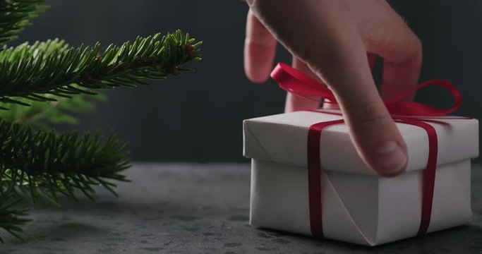 Slow motion man hand put gift box with red ribbon near spruce twig on terrazzo countertop