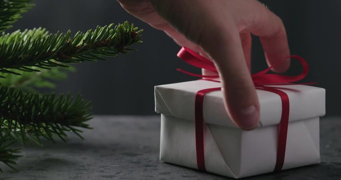 Slow motion man hand put gift box with red ribbon near spruce twig on terrazzo countertop
