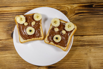 Two sweet sandwiches with delicious chocolate hazelnut spread and banana in shape of bear on wooden table. Top view