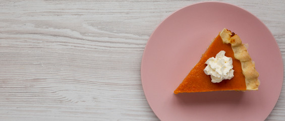Homemade Thanksgiving pumpkin pie on a pink plate on a white wooden background, top view. Overhead, from above, flat lay. Space for text.