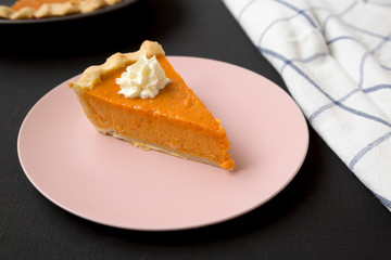 Homemade Thanksgiving pumpkin pie on a pink plate on a black background, side view. Closeup.
