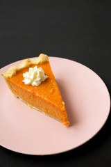 Homemade Thanksgiving pumpkin pie on a pink plate on a black surface, low angle view. Copy space.