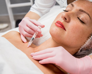 The doctor cosmetologist makes the neckline injections procedure. Young woman in a beauty salon.