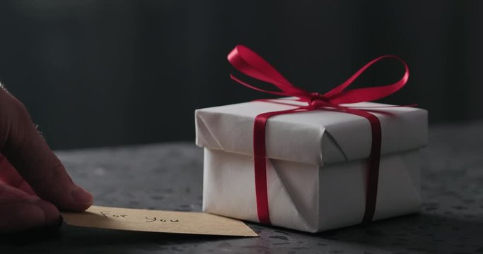 Slow motion man hand put greeting paper card next to white gift box on terrazzo countertop