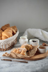 Delicious breakfast concept, close-up. A broken croissant with cream lies on a wooden board, with a honey bowl and a jug of cream.
