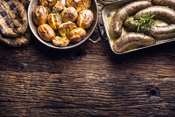 Roasted sausages in pan with rosemary and potatoes.. Traditional european food bratwurst jaternice or jitrnice