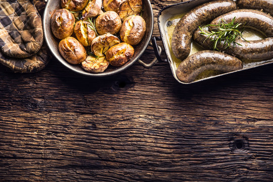 Roasted sausages in pan with rosemary and potatoes.. Traditional european food bratwurst jaternice or jitrnice