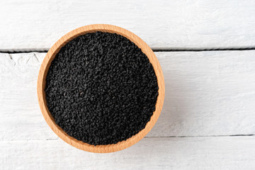 Black cumin seeds in bowl on rustic wooden table. Top view