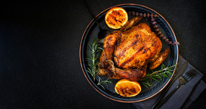 Baked whole chicken with oranges and rosemary. Tray with a festive Christmas dish on a black background. Top view, flatlay. Copyspace
