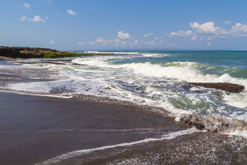 Fototapeta na wymiar Black sand volcanic beach and white waves of ocean in Bali, Indonesia