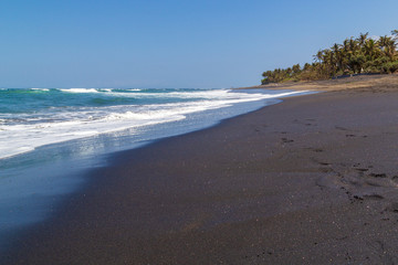 Black sand volcanic beach and white waves of ocean in Bali, Indonesia