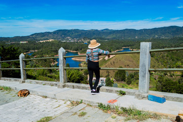 Fototapeta na wymiar Vista trasera de mujer turista con sombrero contemplando la naturaleza en Guatape Colombia desde la piedra del peñol