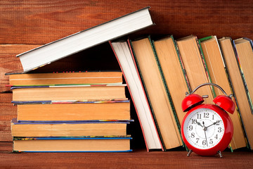 Red clock alarm clock, old books and textbooks on the bookshelf, educational concept.